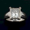 Princess cut diamond ring, weighing 3.41 carats,  in a bezel setting with a tapered baguette to each shoulder. Mounted in whi
