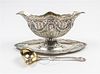 * A German Silver Sauce Boat and Ladle, Late 19th/Early 20th Century, each chased with garlands suspending a central portrait