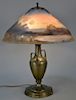 Reverse painted table lamp, The Pairpoint Corp., scenic on metal urn style base. ht. 22 1/2in., dia. 18in. Provenance: Proper
