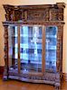 Oak crystal cabinet with carved panel top of carved compote of fruit supported by winged griffins over crystal cabinet with b