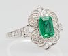 Lady's 18K White Gold Dinner Ring, with a .94 carat emerald atop a pierced lobed border of round diamonds, the sides of the b