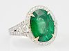 Lady's 18K White Gold Dinner Ring, with an oval 9.25 carat emerald atop a diamond mounted border, the pierced split shoulders