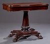 American Carved Mahogany Games Table, 19th c., the serpentine top over a wide skirt, on a tapered octagonal support to a tripodal base on large paw fe