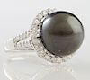 Lady's Platinum Dinner Ring, with a black 16 mm Tahitian cultured pearl within a border of round diamonds, the split sides of the band also mounted wi