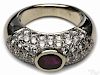 18K white gold, ruby, and diamond ring, centering around a bezel set oval cut ruby