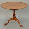Margolis mahogany piecrust tip table with carved top, 
on fluted and carved shaft, set on tripod base ending in ball and claw feet. ...