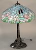 Table lamp having leaded glass shade with flowers and reproduction bronze base, shade is possibly Wilkinson. 