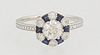 Lady's Platinum Dinner Ring, with a central .51 ct. round diamond atop a border of round diamonds, alternating with baguette sapphires, on a thin reli