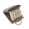 Reloj de viaje marca Orator. Movimiento manual. Caja rectangular en metal base con cubierta de piel color café. Carátula color gris.