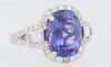 Lady's Platinum Dinner Ring, with an oval 4.45 ct. tanzanite atop a conforming border of round diamonds, with diamond baguette mounted lugs, the split
