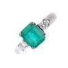 (536613-3-A) An 18ct gold emerald and diamond three-stone ring. The rectangular-shape emerald, with