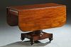 American Empire Carved Mahogany Dropleaf Table, late 19th c., with two rounded corner leaves flanking convex drawers at each end, on a tapered cylindr